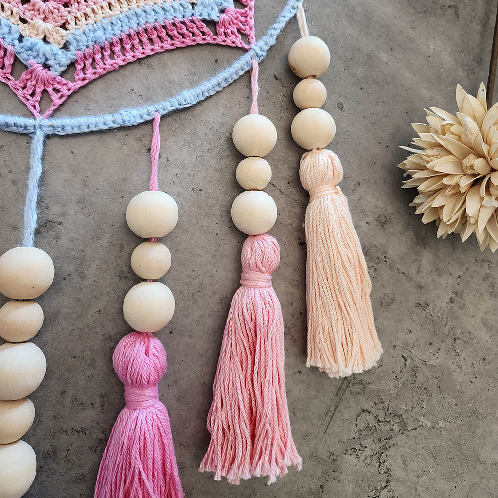 "Dreamscape" by ArtixHub – macramé wall hanging with pastel pink and blue tassels accented by natural wood beads, creating a playful cascade of color and texture. Ideal for nurseries, playrooms, or boho-inspired living spaces, adding whimsical charm to UAE interiors.